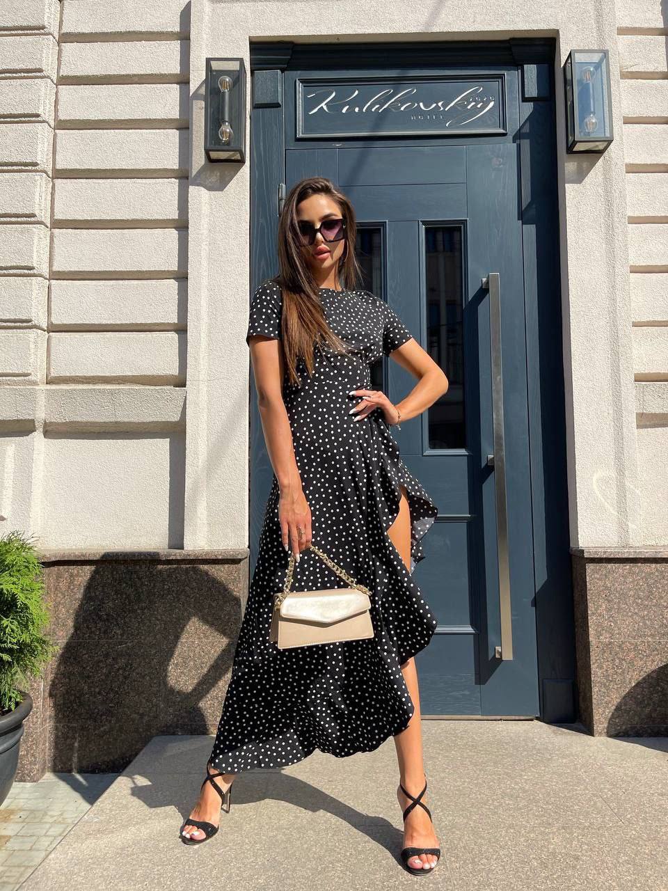 Woman in a black polka dot dress standing in front of a blue door with 'Kobbeberg' sign.