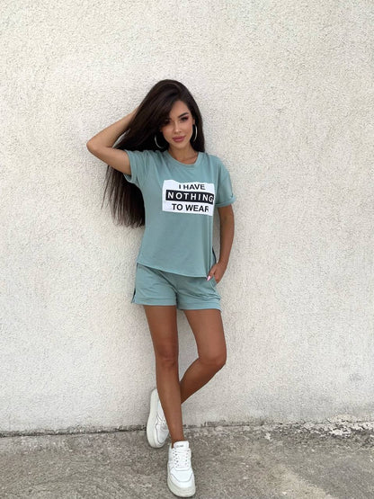Woman wearing a light blue t-shirt with text and matching shorts against a textured wall.