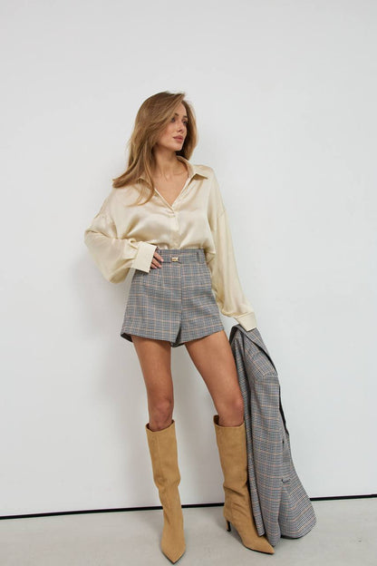 Woman wearing a beige blouse, plaid skirt, and tan boots against a white background
