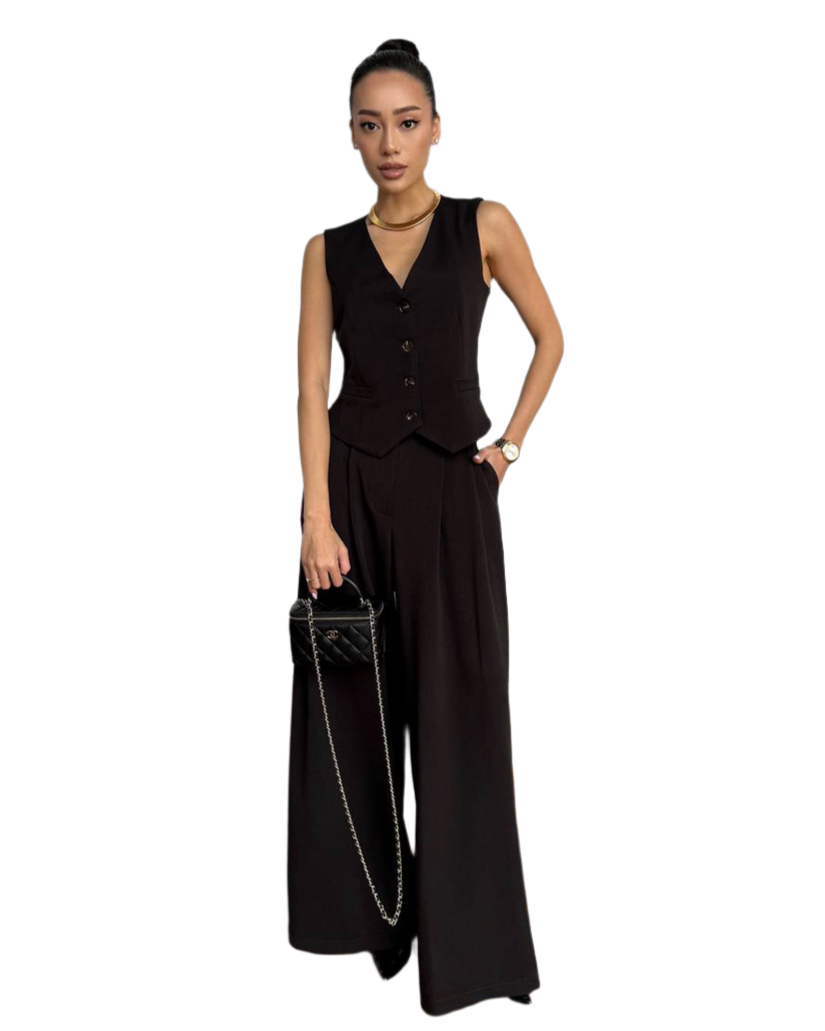 Woman wearing a black sleeveless jumpsuit holding a handbag on a white background