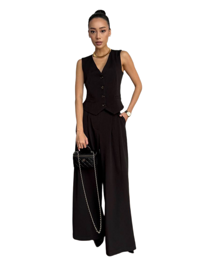 Woman wearing a black sleeveless jumpsuit holding a handbag on a white background