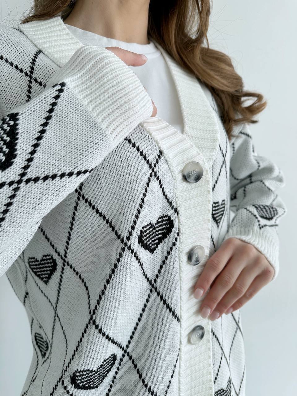 White cardigan with black heart patterns and button details on a white background