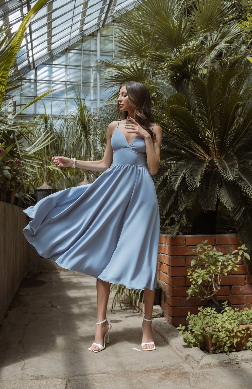 Woman in a light blue dress standing in a greenhouse with plants around