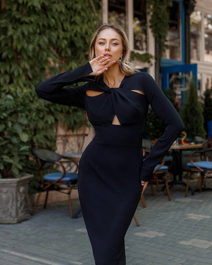 Woman in a black dress standing outdoors with greenery and tables in the background
