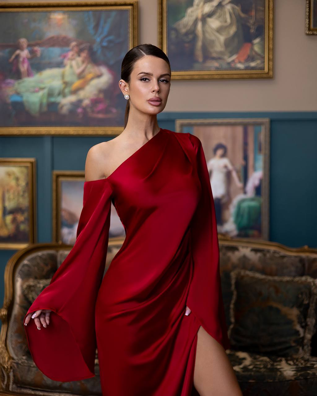 Woman in a red dress standing in an ornate room with classical paintings on the wall.