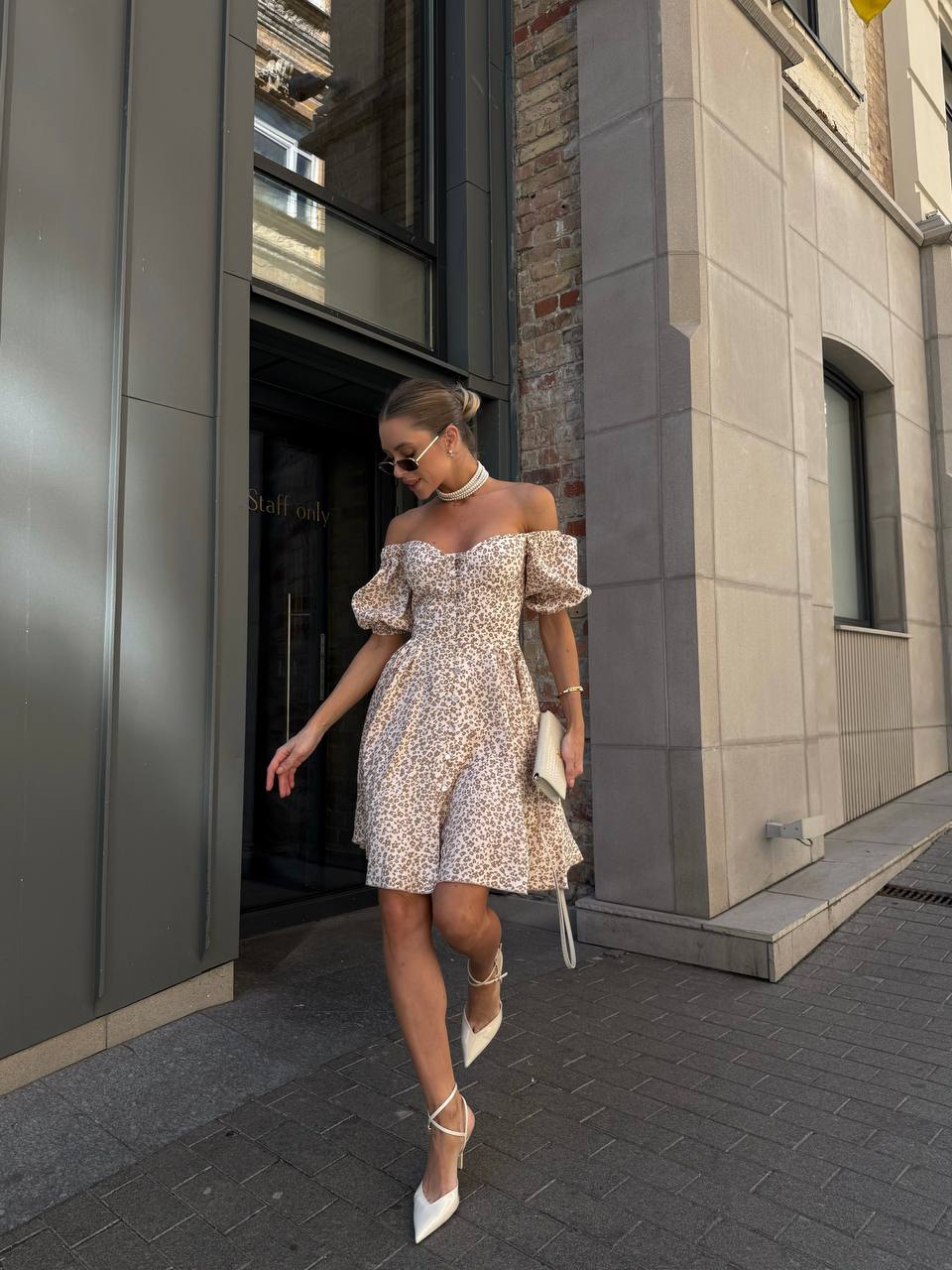 Woman in a floral off-shoulder dress walking outside a building.