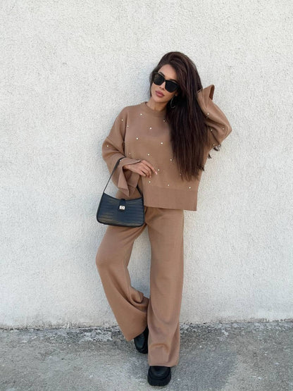 Woman in a beige outfit with a black handbag against a white wall