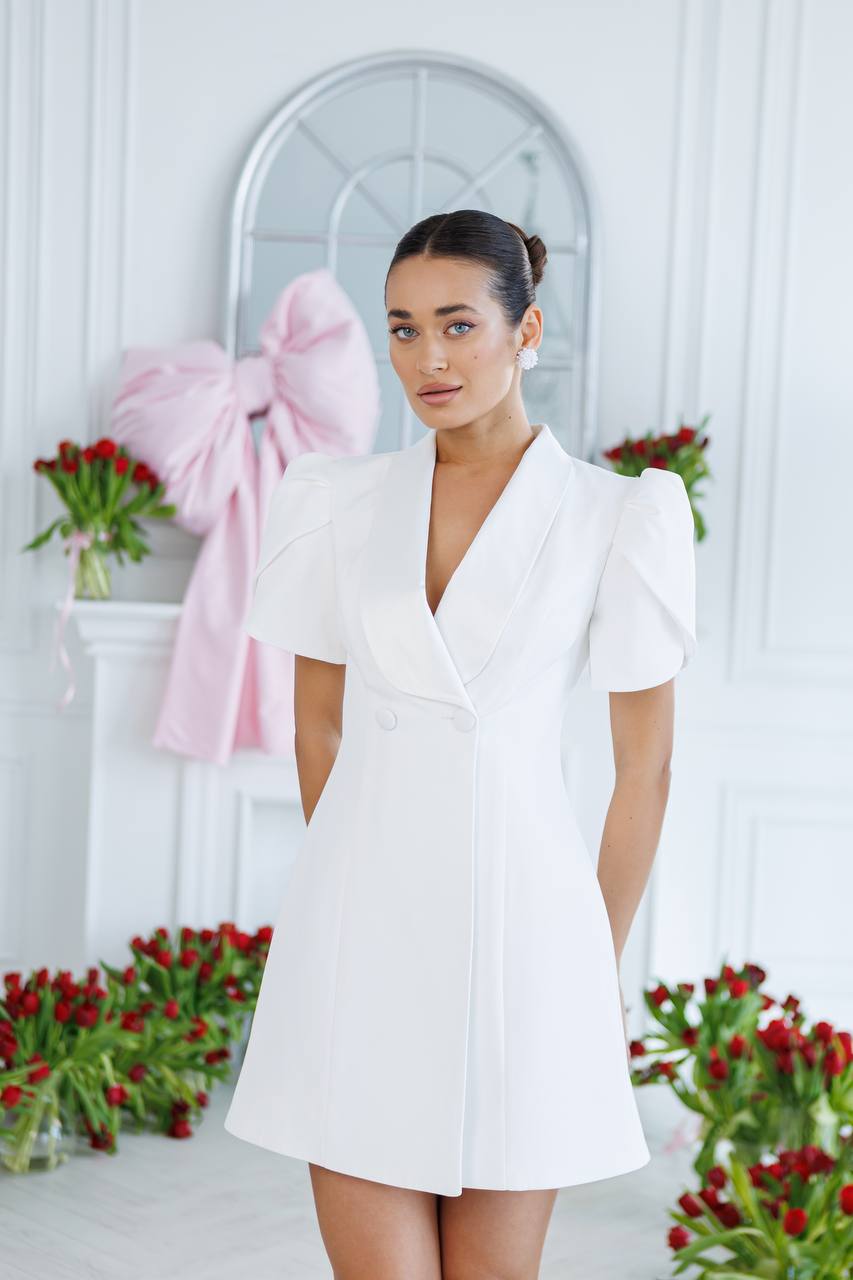 Woman in a white dress standing in a decorated room with flowers and a pink bow.
