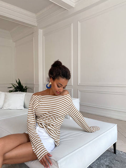 Woman sitting on a white couch wearing a striped sweater in a room with white paneled walls.