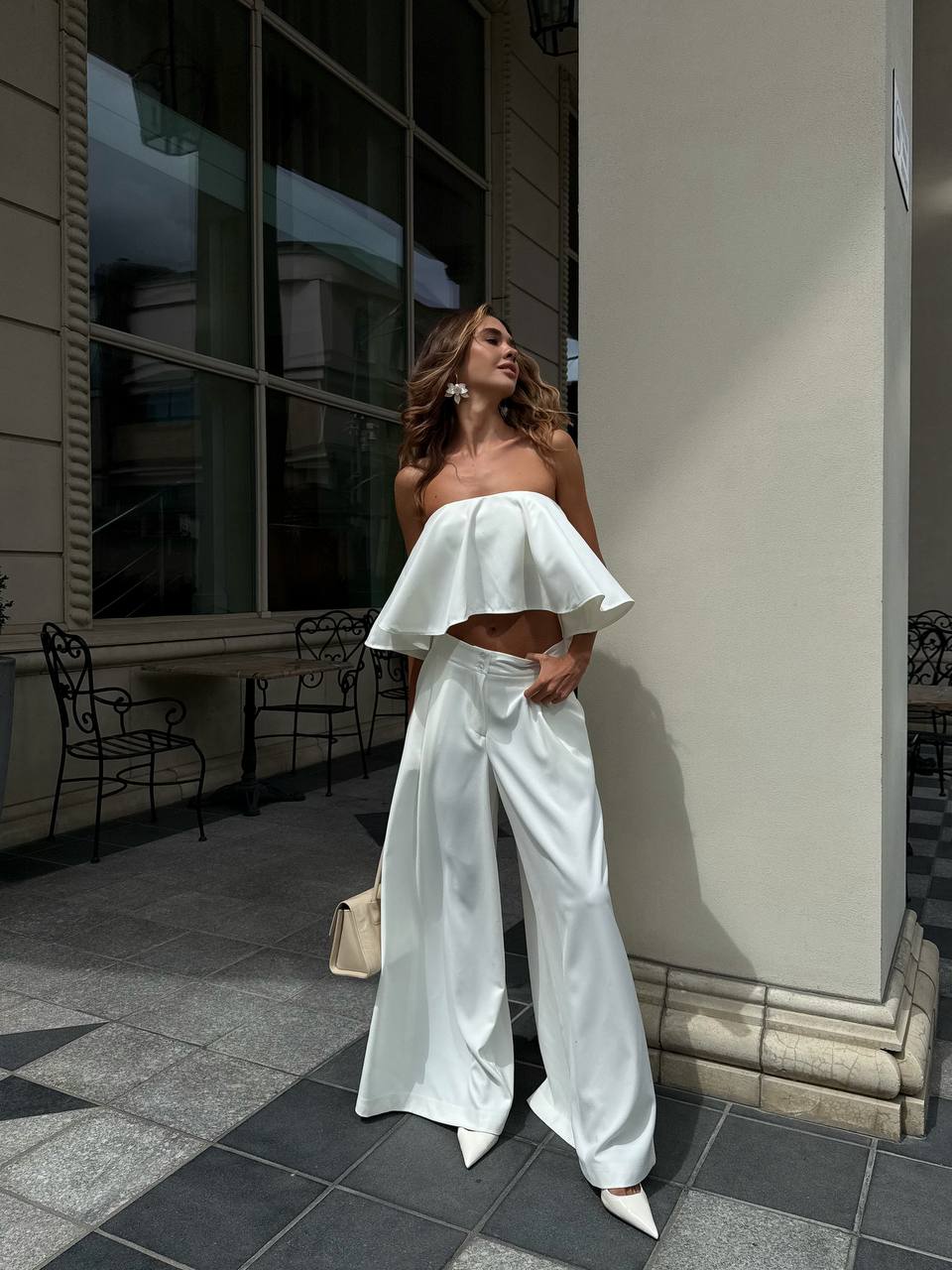 Woman in a white outfit standing on a sidewalk with a building in the background
