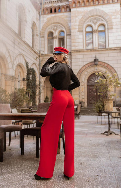 Person wearing a black top and red pants standing in an outdoor setting with architectural background