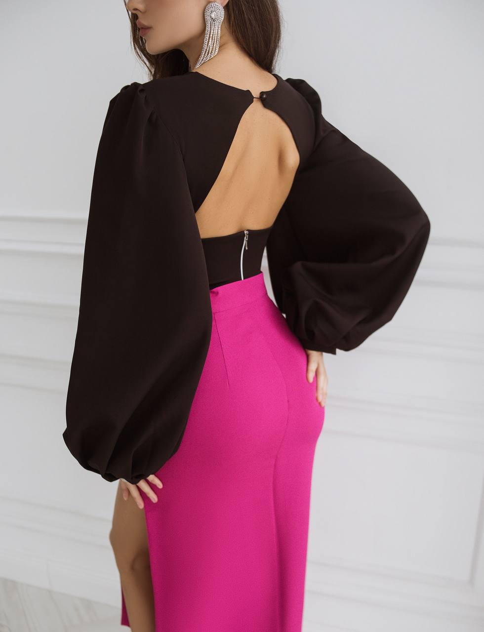 Person wearing a black top with cut-out design and pink pants against a white background