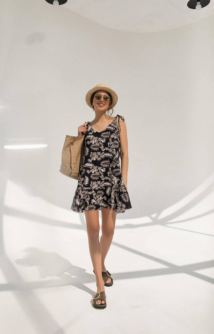 Woman wearing a floral dress and straw hat holding a bag on a white background