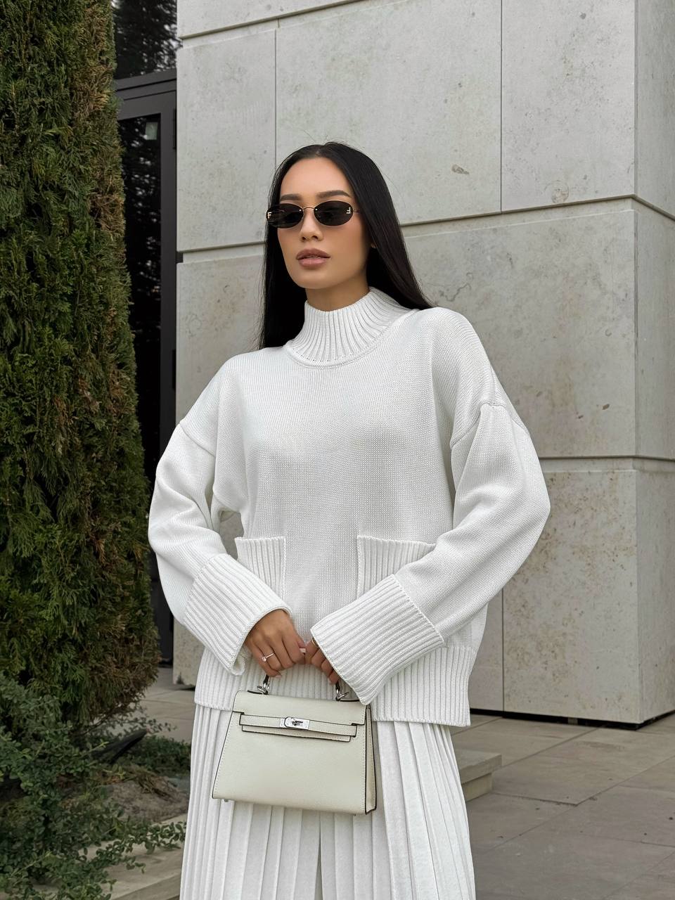 Woman wearing a white sweater and skirt with sunglasses, standing outdoors.