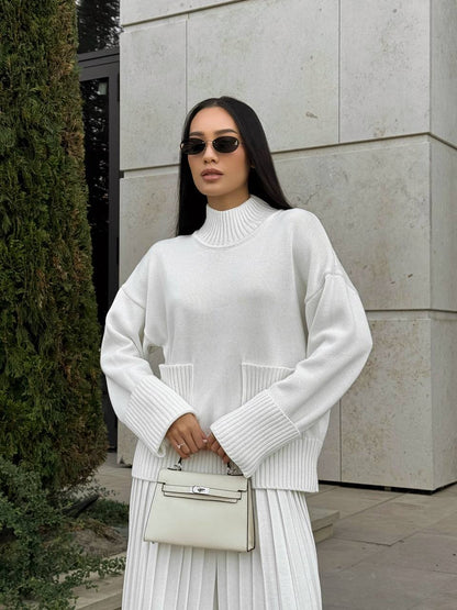 Woman wearing a white sweater and skirt with sunglasses, standing outdoors.