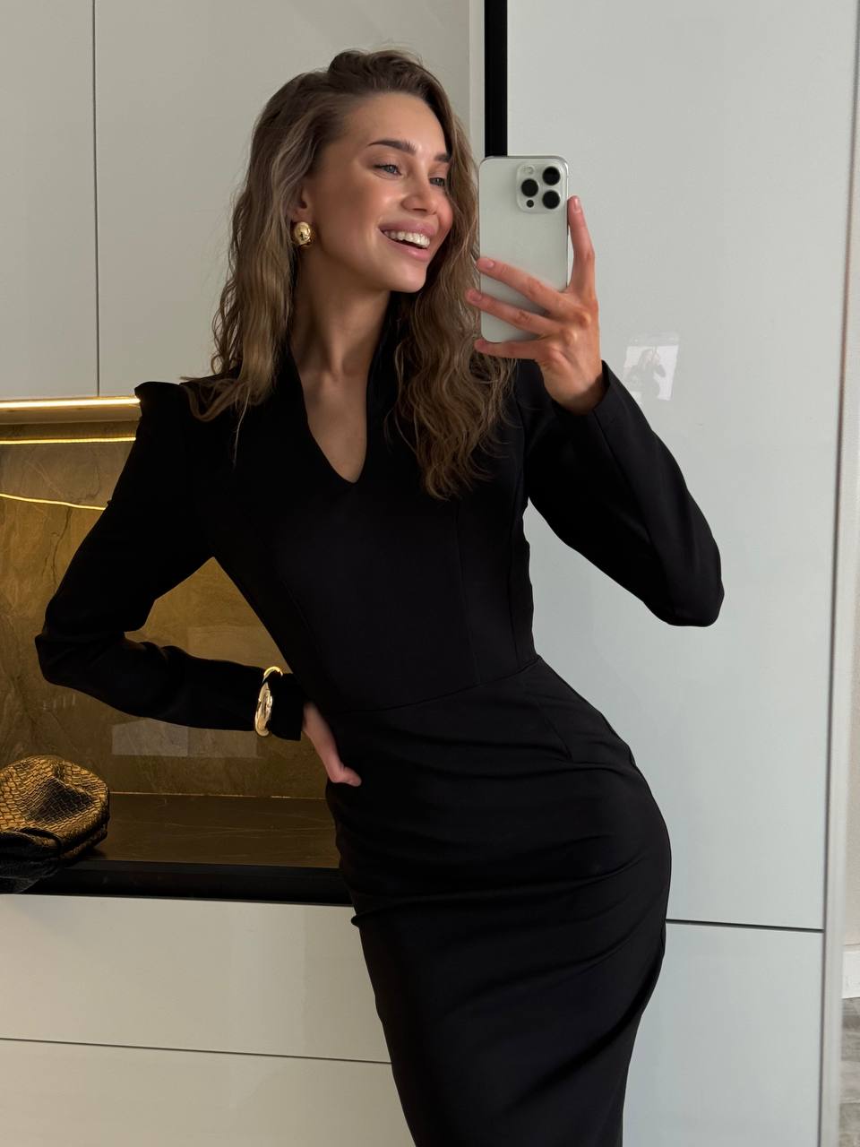 Woman taking a mirror selfie wearing a black dress in an indoor setting.