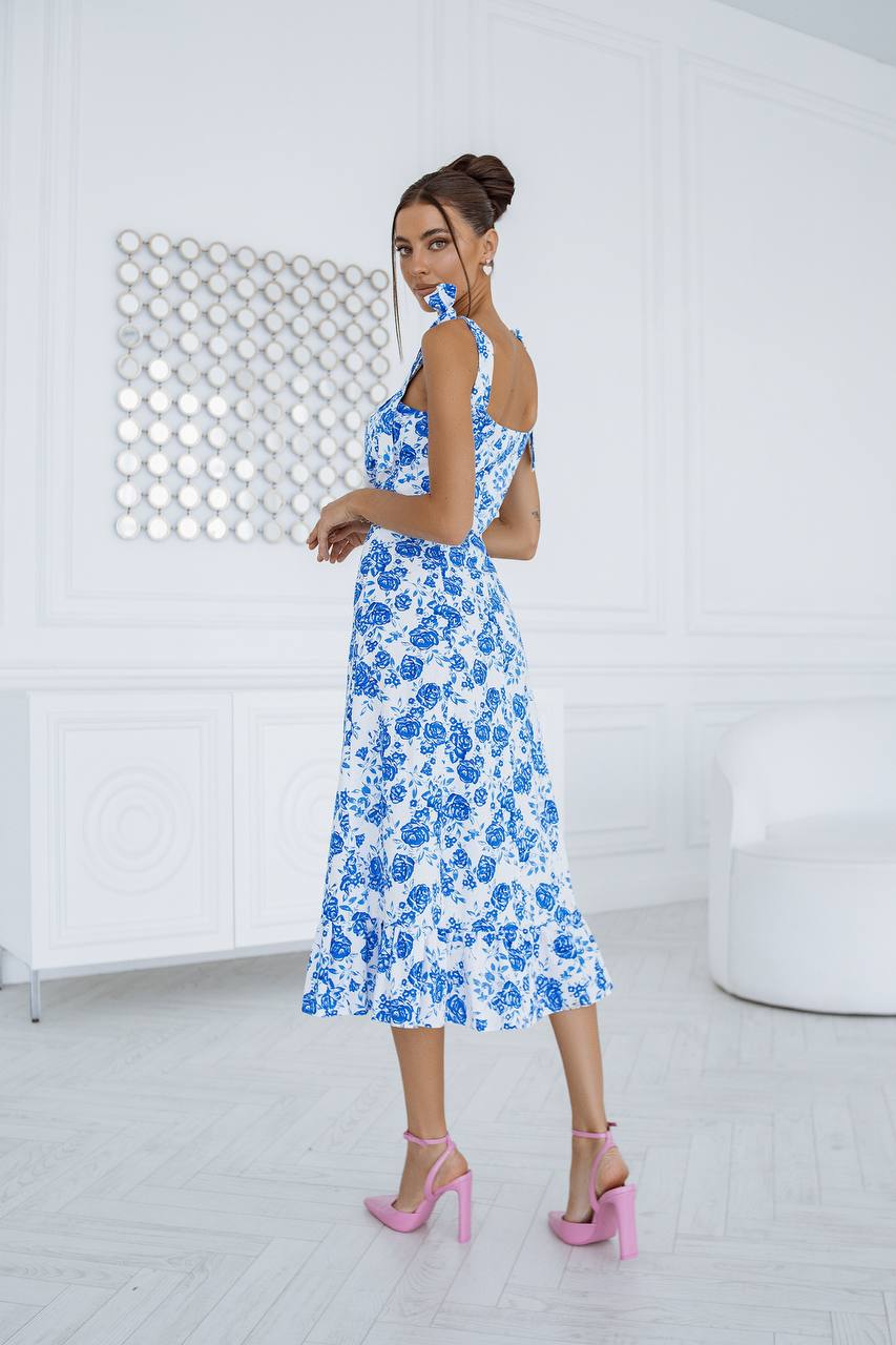 Woman in a blue floral dress standing in a minimalistic room with white walls and floor.