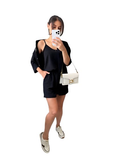 Woman taking a mirror selfie wearing a black outfit with a white handbag on a white background