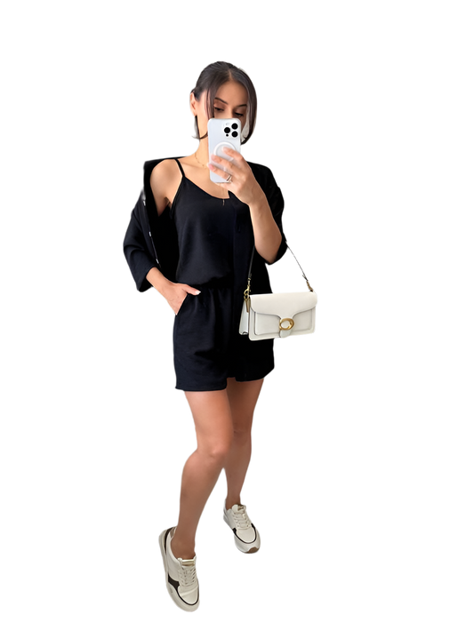 Woman taking a mirror selfie wearing a black outfit with a white handbag on a white background