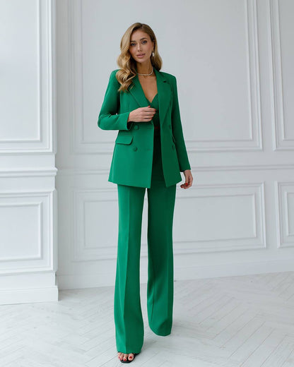 Woman wearing a green suit standing against a white wall.
