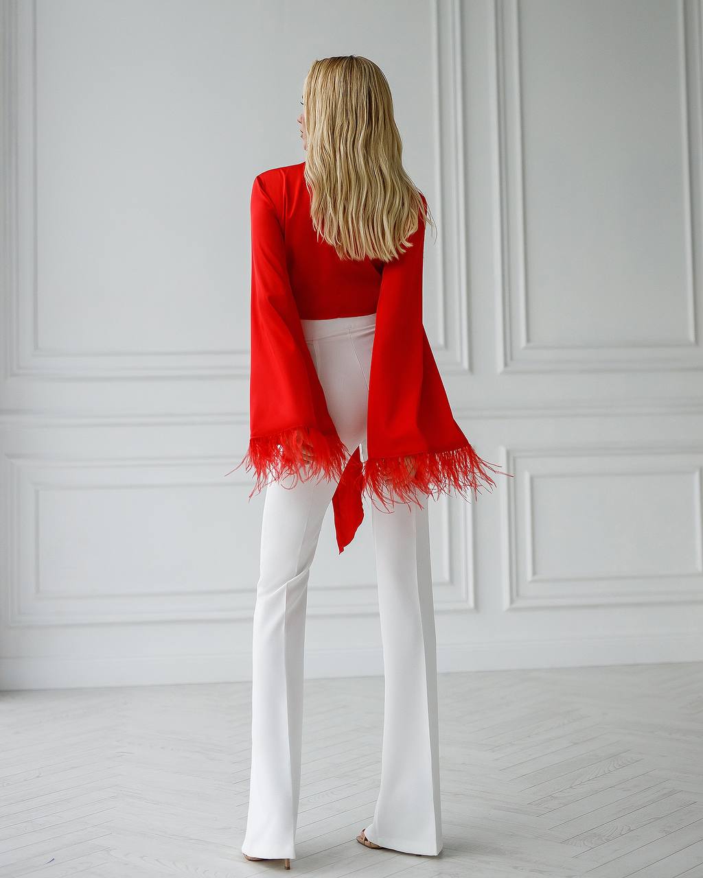 Person wearing a red scarf and white pants against a white wall.