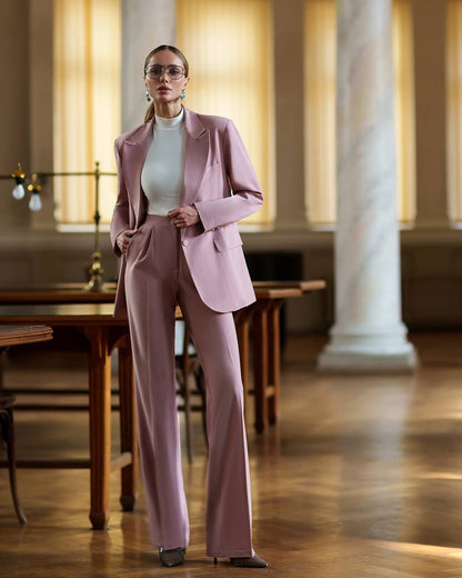 Woman in a pink suit standing in an elegant room with wooden tables and columns.