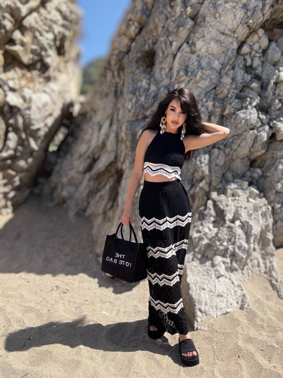 Woman in black and white outfit standing against rocky background