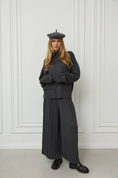 Person wearing a dark gray outfit with a beret against a white paneled wall.