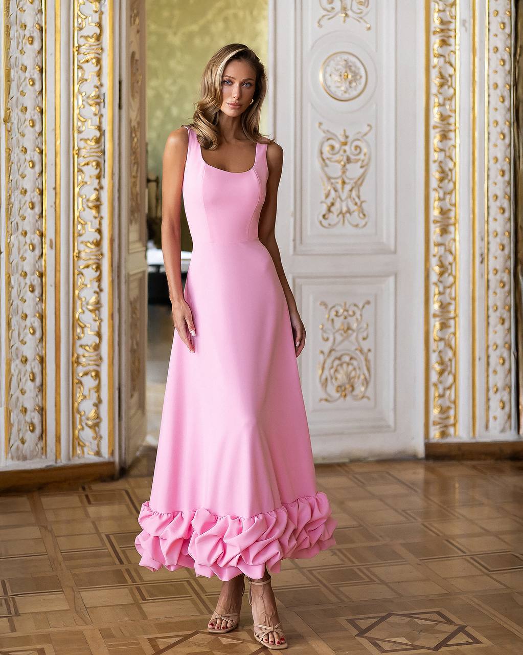 Woman wearing a pink dress with ruffled hem in an ornate room.