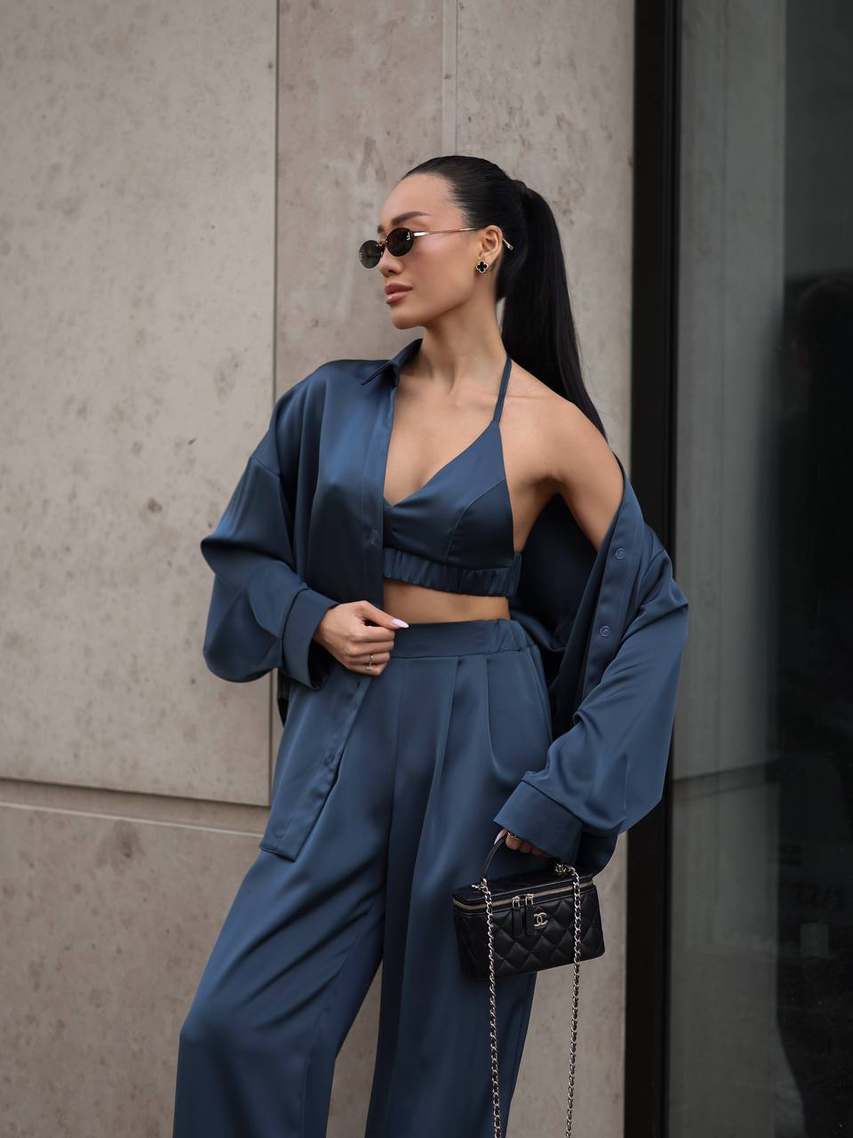 Woman in a blue outfit standing against a neutral wall.