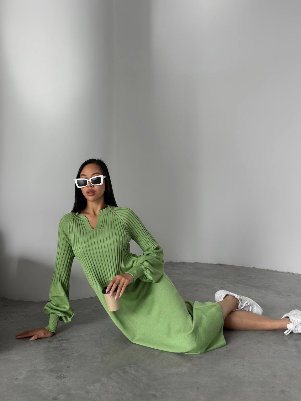 Woman in a green dress sitting on the floor against a plain background