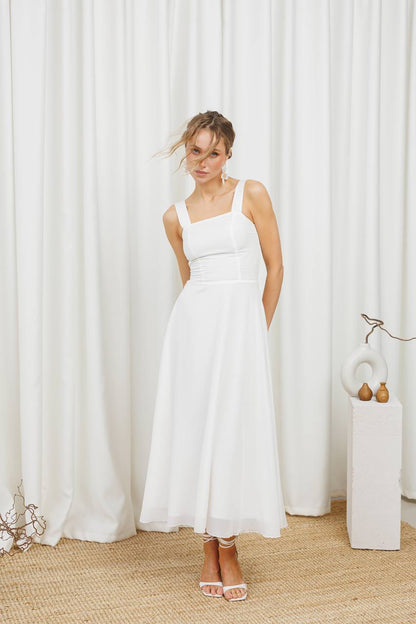 Woman wearing a white dress standing in front of white curtains