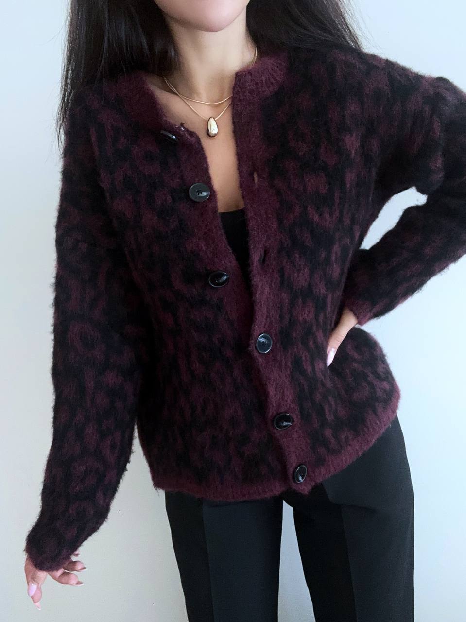 Person wearing a dark purple cardigan with a leopard print pattern on a plain background
