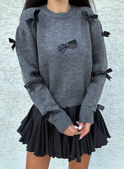 Gray sweater with black ribbons and a black pleated skirt on a light gray background