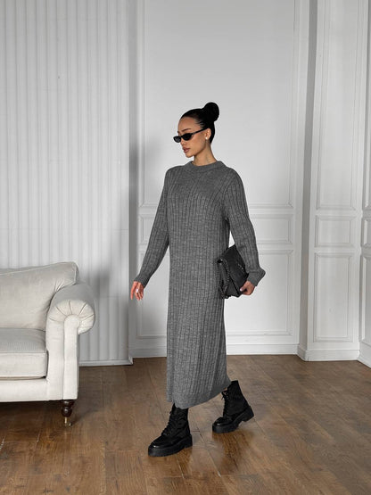 Woman in a gray knit dress standing in a room with white walls and a gray sofa.