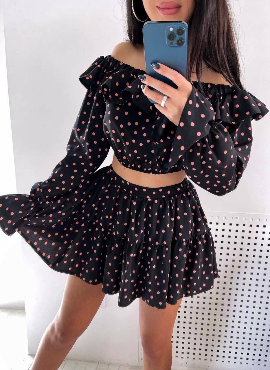 Person wearing a black polka dot outfit with long sleeves and a skirt, holding a phone.