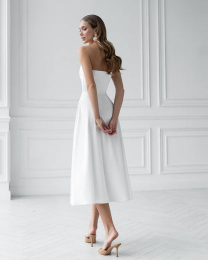 Woman wearing a white strapless dress against a white wall