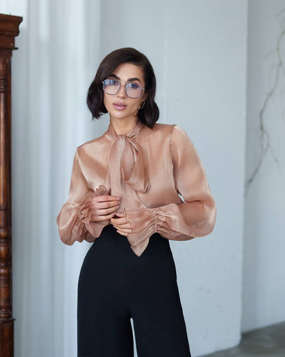 Woman wearing a sheer beige blouse with a white wall background