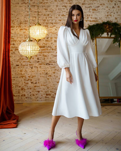 Woman in a white dress standing in a room with brick walls and hanging lights.