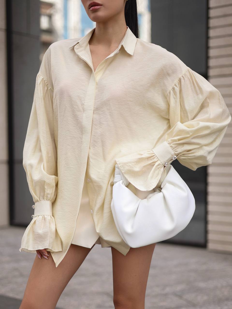 Person wearing a light-colored shirt and holding a white handbag outdoors.