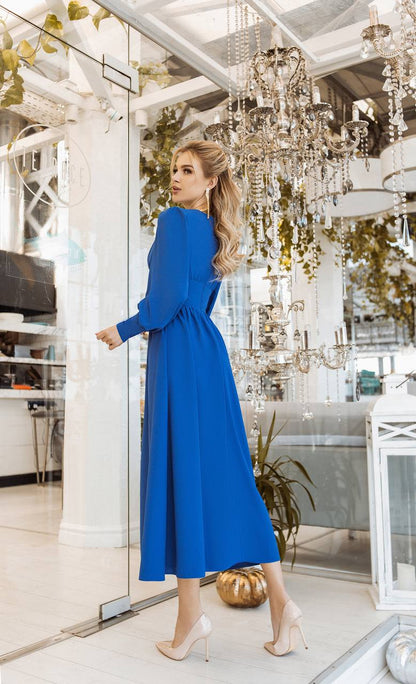 Woman in a blue dress standing in a stylish interior setting with chandeliers.
