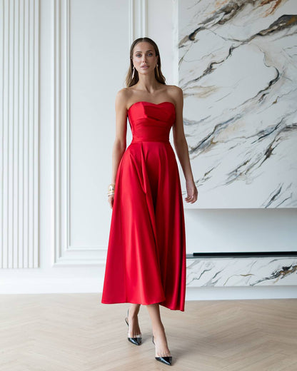 Woman wearing a red strapless dress in a room with marble wall.