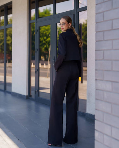 Woman in a black outfit standing outside a building with large glass doors.