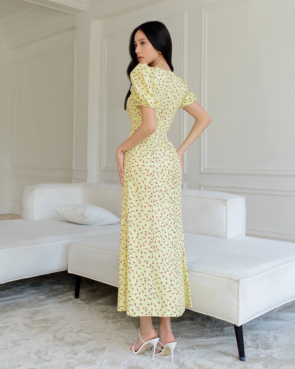 Woman in a yellow floral dress standing in a modern room with white furniture.