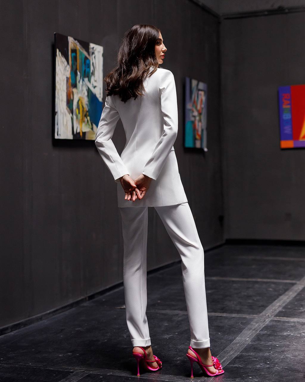 Woman in a white suit with pink high heels standing in an art gallery.
