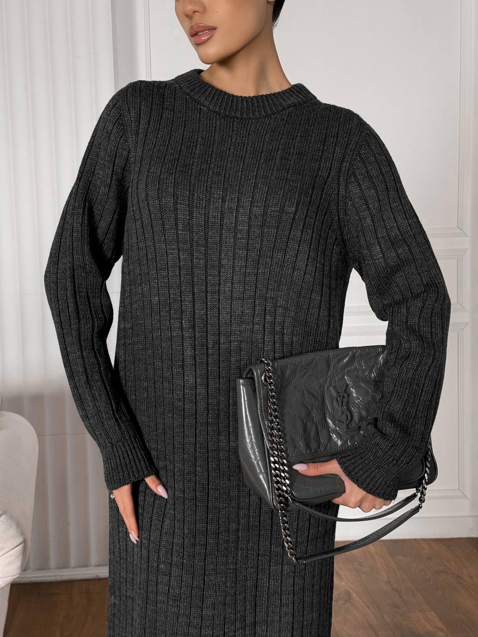 Woman wearing a black ribbed sweater and holding a black clutch.