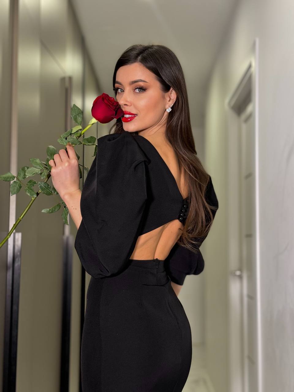 Woman in a black dress holding a red rose in an elevator.