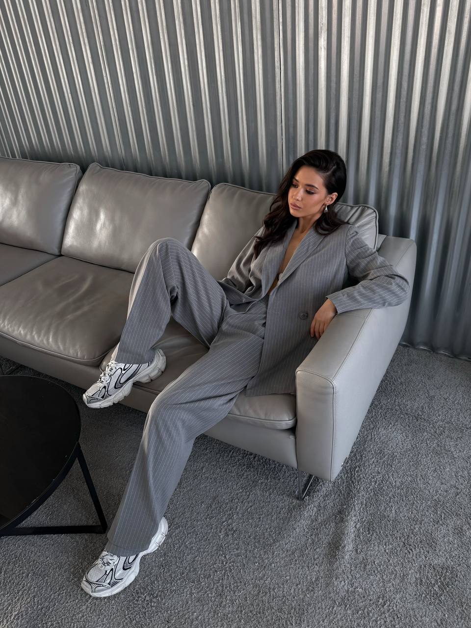 Woman in a gray suit sitting on a gray sofa in a modern interior setting.