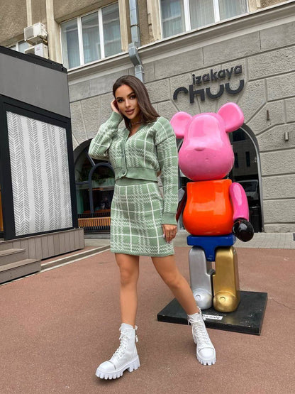 Woman in a green outfit standing next to a colorful bear sculpture in an urban setting.