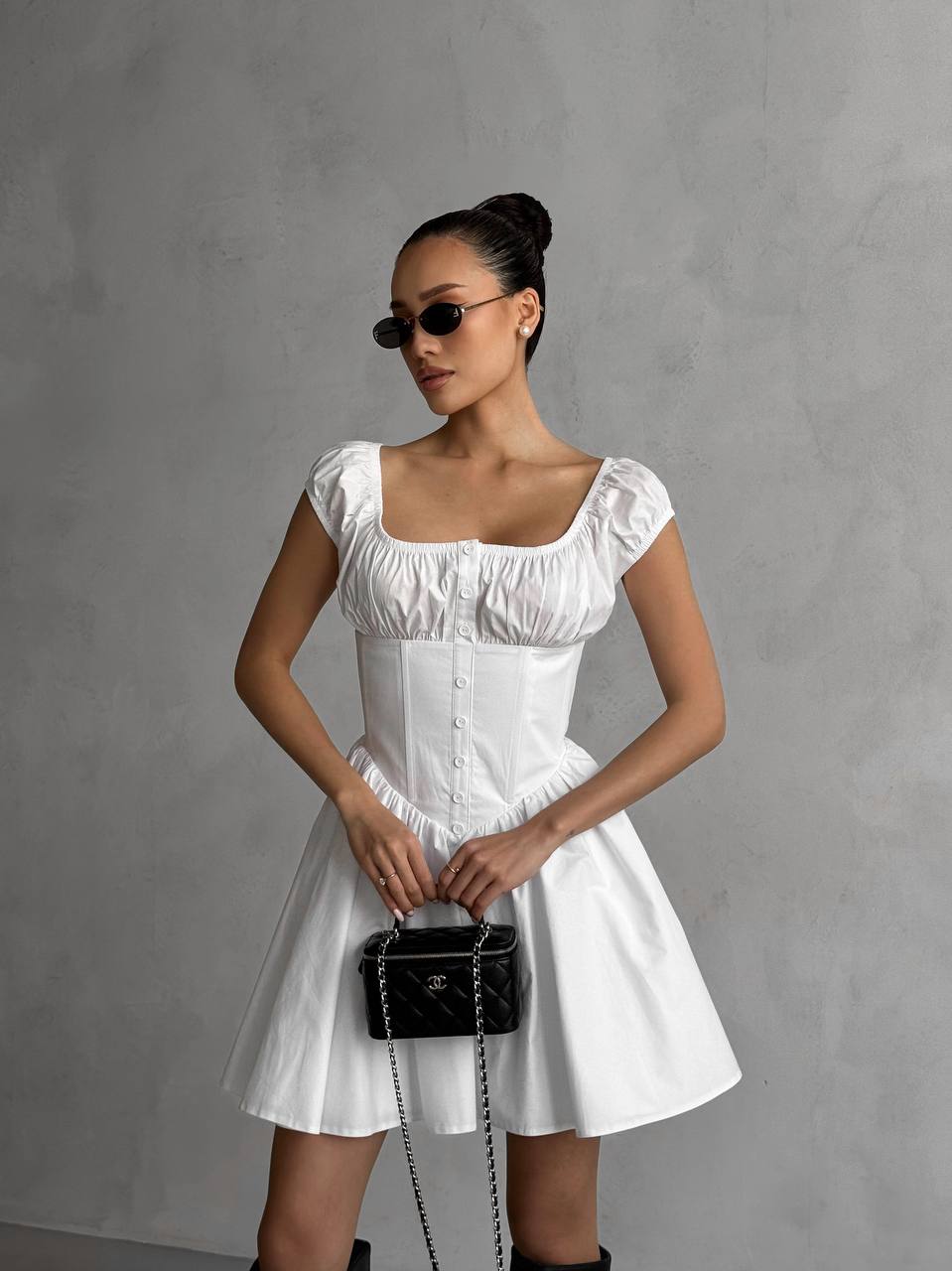 Woman in a white dress holding a black handbag against a gray background